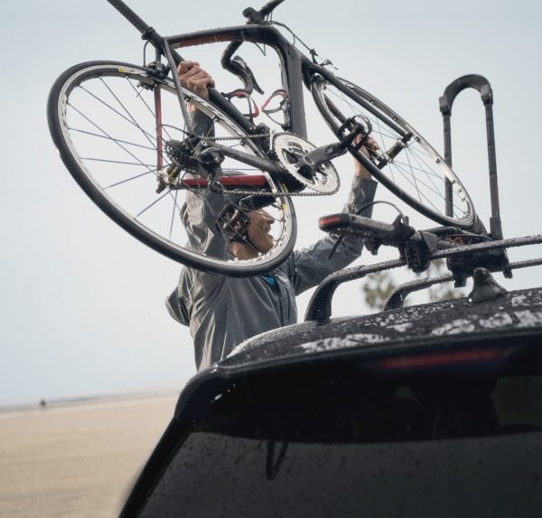 Un homme qui fixe son vélo sur les longerons de toit d’un coupé multisegment INFINITI