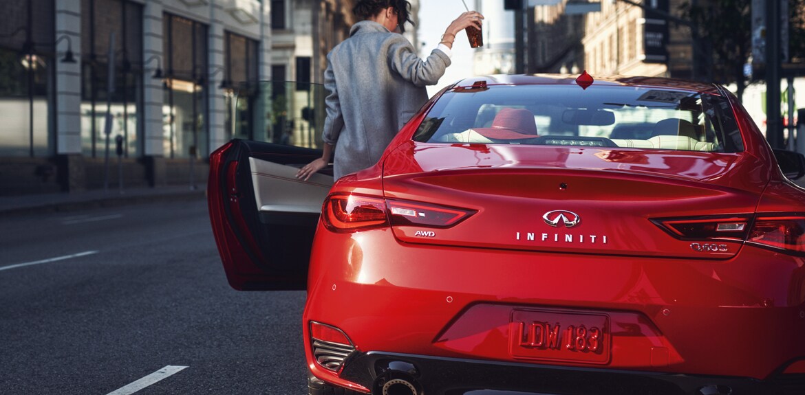 Vue arrière d’une femme entrant dans sa voiture qui est un coupé sport INFINITI Q60 S 2022 rouge